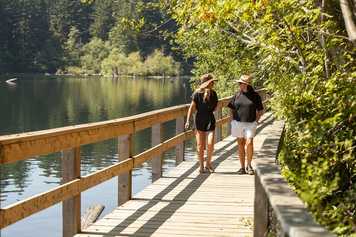 A man and woman hiking on a wooden bridge next to water